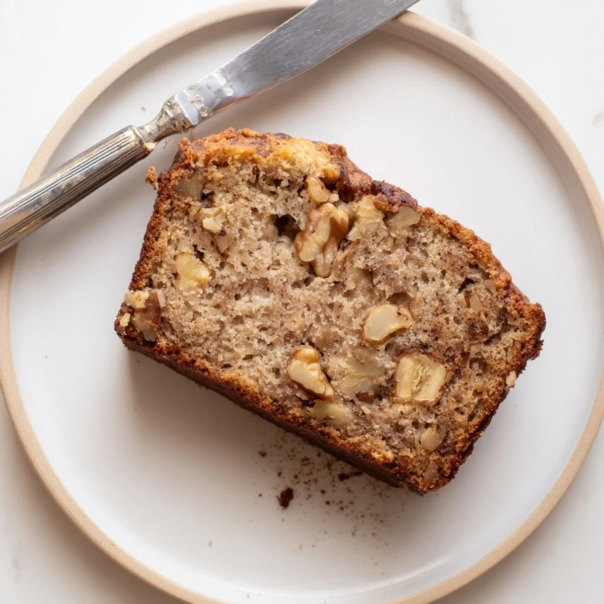 A slice of moist Banana Bread on a white plate, topped with melting butter, ready for breakfast or snack.