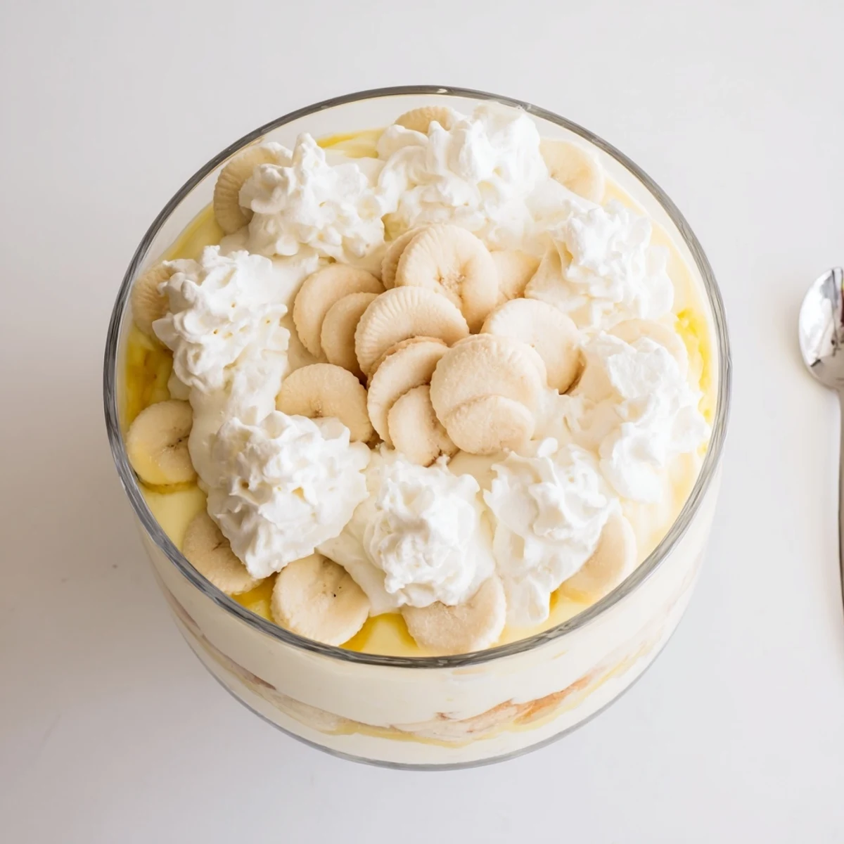 A spoon lifts a serving of Banana Pudding from the dish, revealing fluffy whipped cream topping and soft layers.