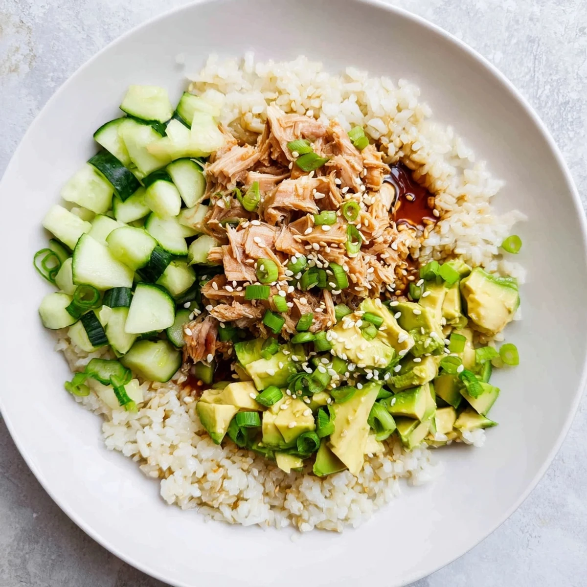 A vibrant Tuna Avocado Rice Bowl features crisp cucumber, scallions, and toasted sesame seeds for a satisfying, textured meal.  