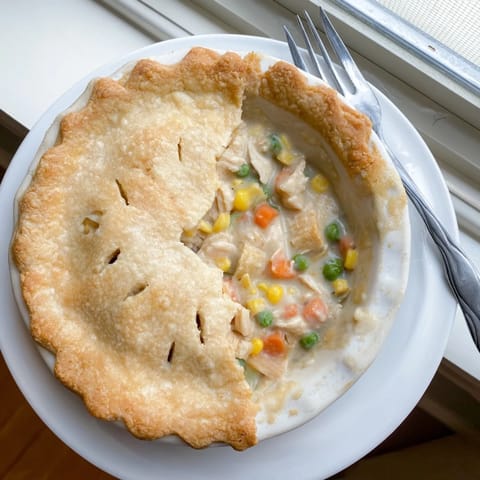 Freshly baked Chicken Pot Pie sits beside a green salad on a rustic wooden table.