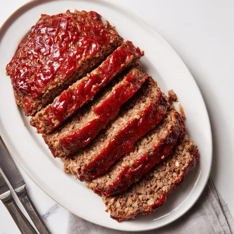 A tender, juicy slice of homemade meatloaf featuring a tangy glaze, paired with green beans and mashed potatoes for dinner.