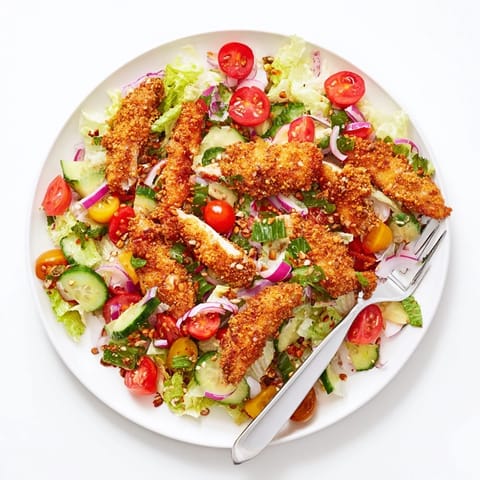A close-up of Crispy Hot Honey Chicken Salad highlights crunchy seed garnishes and bright cherry tomatoes on fresh lettuce.