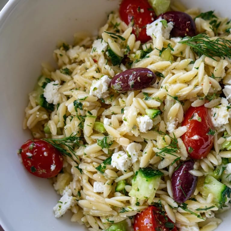 Greek Orzo Salad served chilled with juicy tomatoes, crunchy cucumbers, and tangy feta, perfect for picnics.