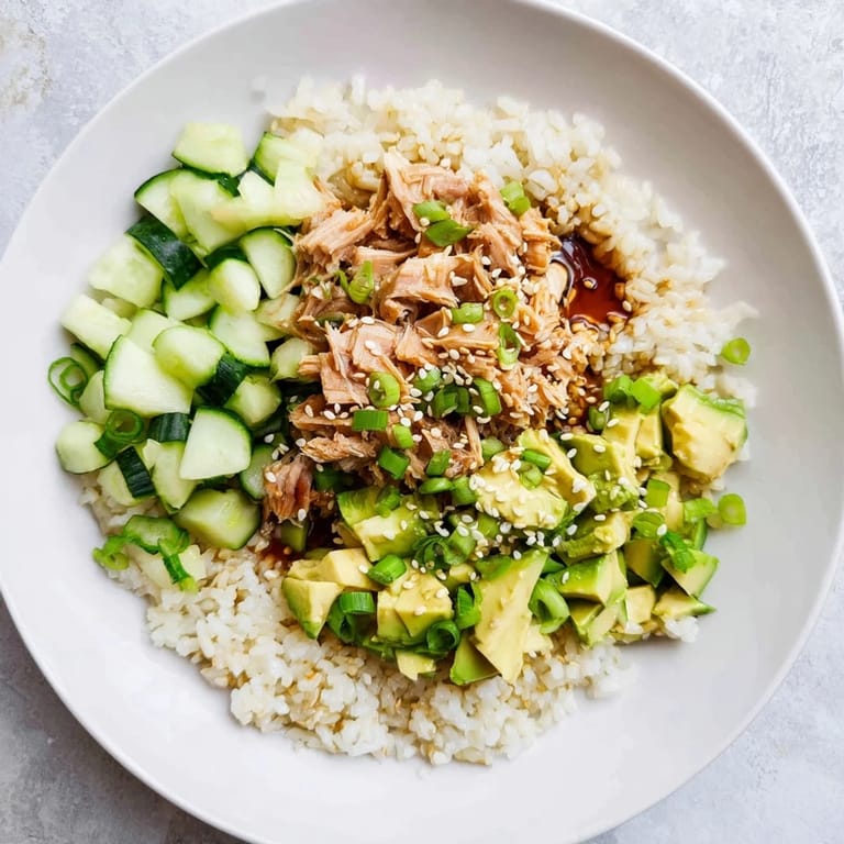 A vibrant Tuna Avocado Rice Bowl features crisp cucumber, scallions, and toasted sesame seeds for a satisfying, textured meal.  