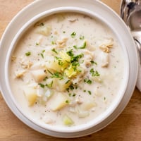 Creamy New England Clam Chowder in a rustic bowl, steam rising, served with oyster crackers and a parsley garnish for a cozy meal.